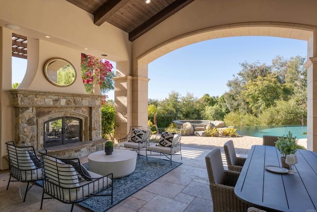 view of patio with a hot tub and an outdoor stone fireplace