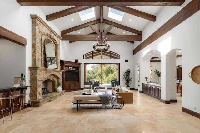 living room featuring a stone fireplace, a skylight, a chandelier, high vaulted ceiling, and beam ceiling