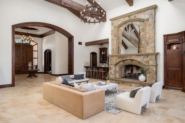 living room with crown molding, a notable chandelier, a stone fireplace, and a towering ceiling