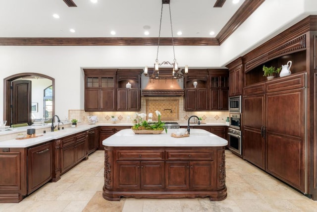 kitchen with sink, hanging light fixtures, stainless steel appliances, tasteful backsplash, and an island with sink