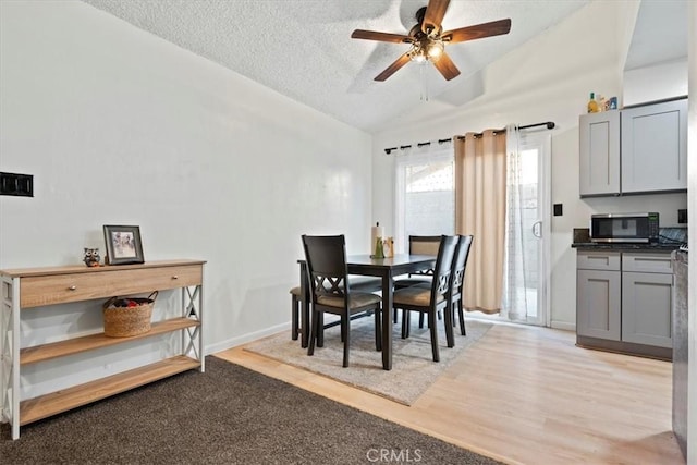 dining area featuring ceiling fan, lofted ceiling, light hardwood / wood-style floors, and a textured ceiling