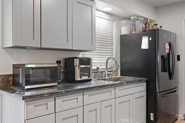 kitchen with stainless steel appliances, sink, white cabinets, and dark stone counters