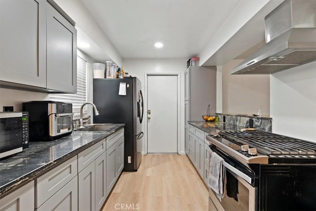 kitchen featuring sink, appliances with stainless steel finishes, dark stone countertops, light hardwood / wood-style floors, and wall chimney exhaust hood