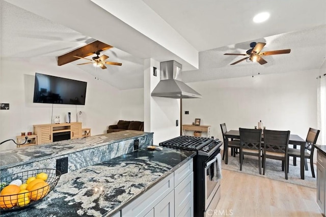 kitchen featuring wall chimney exhaust hood, gas stove, vaulted ceiling with beams, light wood-type flooring, and dark stone counters