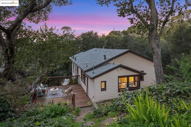 back house at dusk featuring a wooden deck and a fire pit