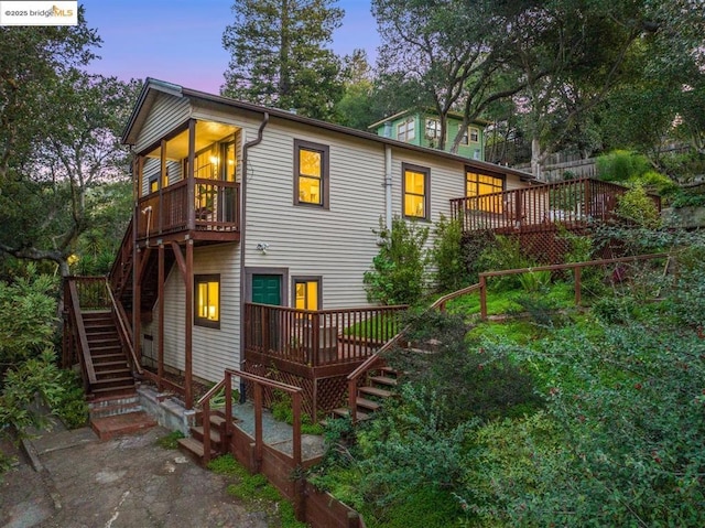 back house at dusk featuring a wooden deck and a sunroom