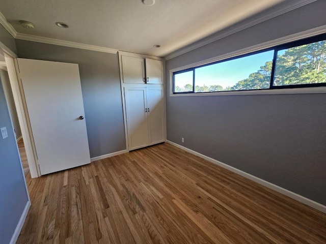 unfurnished bedroom featuring wood-type flooring, crown molding, and a closet