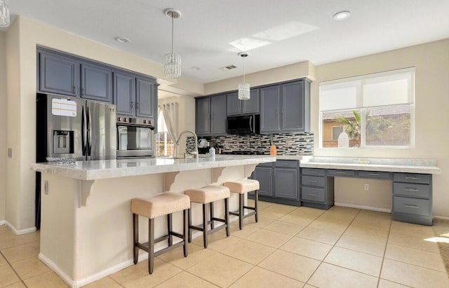 kitchen with decorative backsplash, light tile patterned flooring, stainless steel appliances, and a center island with sink