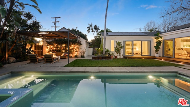 pool at dusk featuring a patio, outdoor lounge area, and a lawn