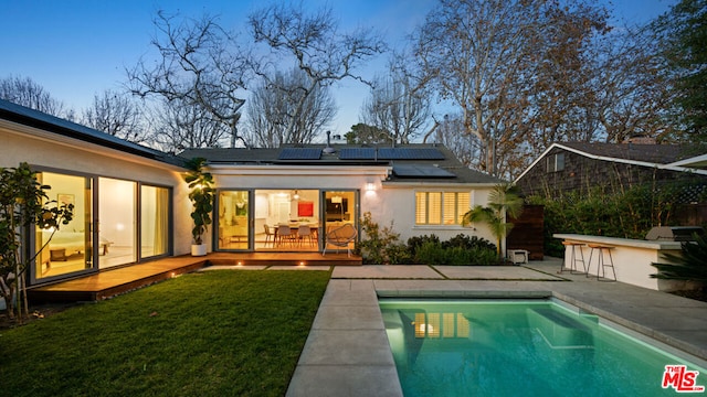 back house at dusk featuring a swimming pool side deck, a yard, a patio, and exterior bar