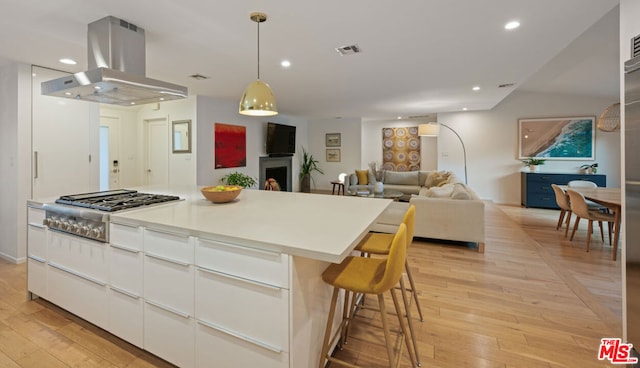 kitchen with white cabinetry, hanging light fixtures, island range hood, stainless steel gas cooktop, and a kitchen island