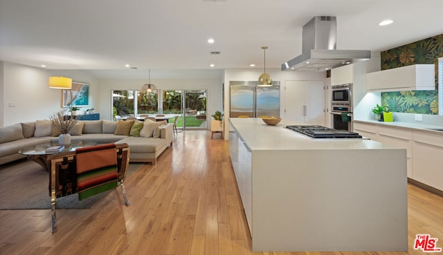 kitchen featuring appliances with stainless steel finishes, white cabinetry, a center island, island range hood, and decorative light fixtures