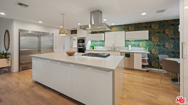 kitchen featuring white cabinetry, island range hood, built in appliances, a center island, and decorative light fixtures