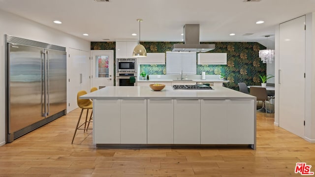 kitchen featuring island range hood, built in appliances, decorative light fixtures, and white cabinets