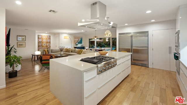 kitchen with white cabinetry, island range hood, a center island, appliances with stainless steel finishes, and pendant lighting