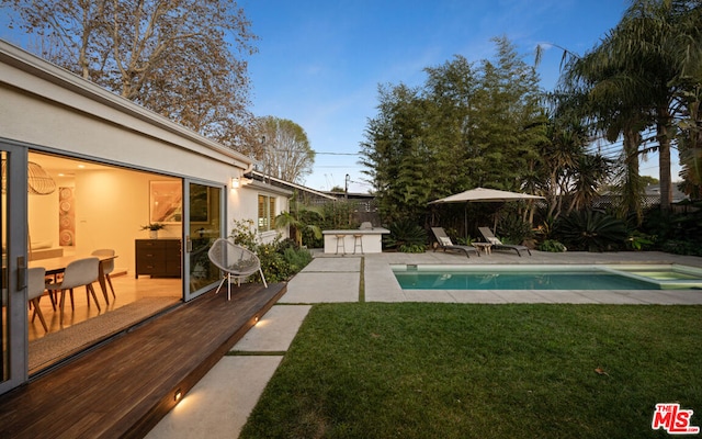 pool at dusk featuring exterior bar and a yard