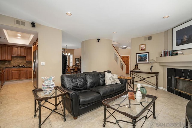 tiled living room with a raised ceiling, a chandelier, and a fireplace