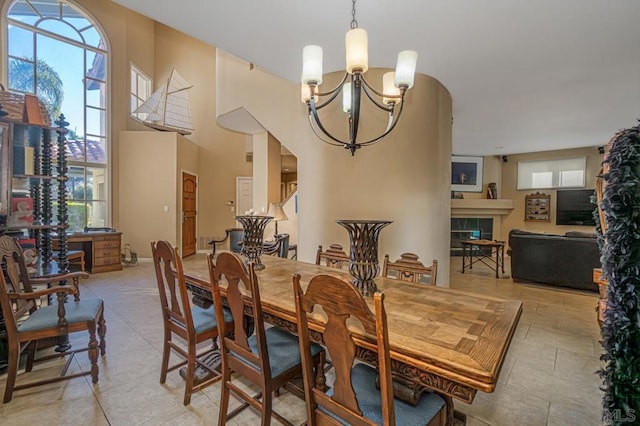 dining room with a high ceiling, light tile patterned floors, a tile fireplace, and a notable chandelier