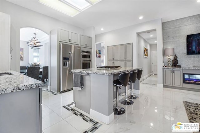 kitchen featuring a kitchen bar, appliances with stainless steel finishes, gray cabinets, a kitchen island, and pendant lighting