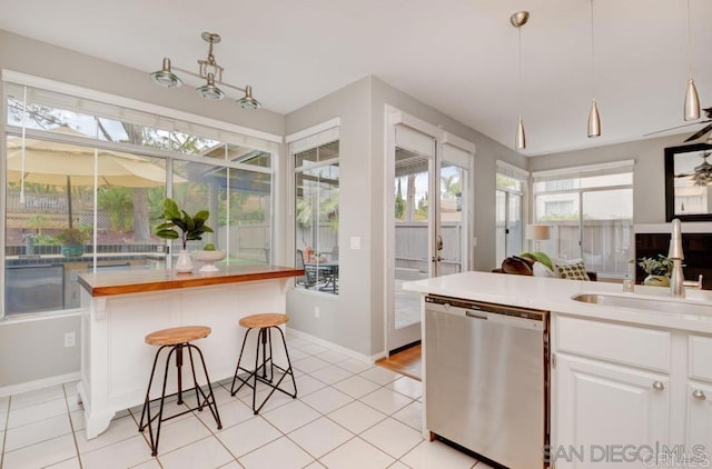 kitchen with hanging light fixtures, white cabinetry, stainless steel dishwasher, and wood counters