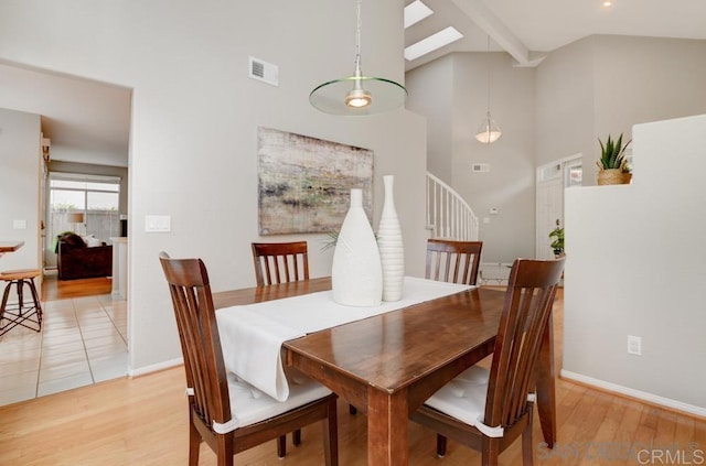 dining area featuring beam ceiling, high vaulted ceiling, and light hardwood / wood-style flooring