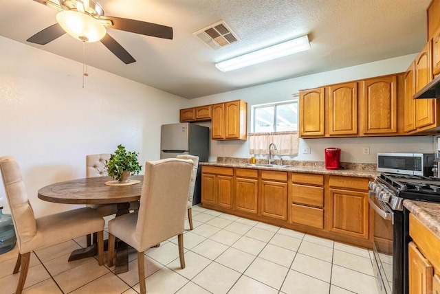 kitchen with light tile patterned flooring, appliances with stainless steel finishes, sink, light stone countertops, and a textured ceiling