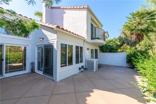 rear view of house featuring a patio, stucco siding, fence, a balcony, and a tiled roof