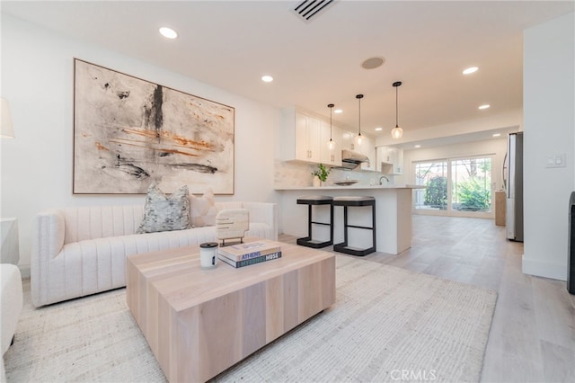 living area with light wood-style floors, visible vents, and recessed lighting