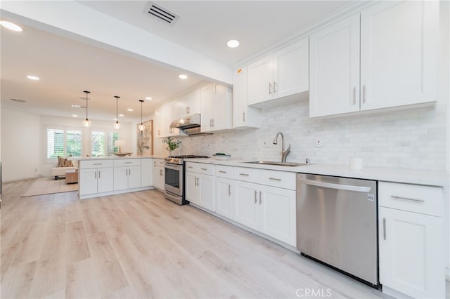 kitchen featuring appliances with stainless steel finishes, decorative light fixtures, light countertops, white cabinetry, and a sink