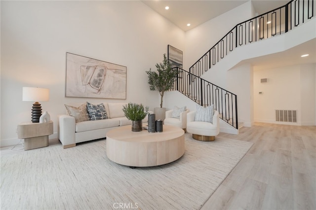 living area featuring a high ceiling, wood finished floors, visible vents, baseboards, and stairway