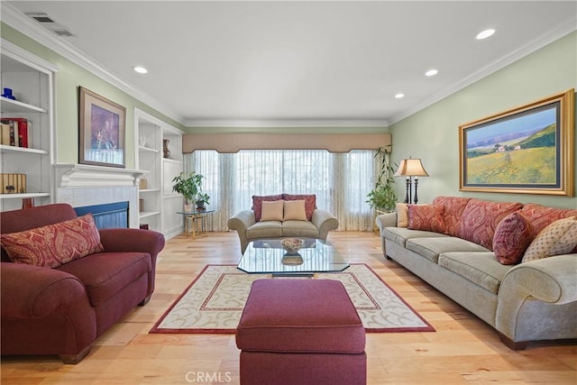 living room featuring a tile fireplace, ornamental molding, built in features, and light hardwood / wood-style floors