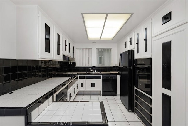 kitchen with tasteful backsplash, tile countertops, black appliances, and white cabinets