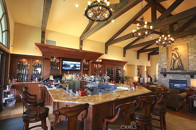 bar featuring light stone counters, a fireplace, high vaulted ceiling, and a chandelier