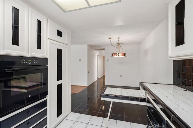 kitchen featuring dark tile patterned floors, double oven, tile counters, white cabinets, and decorative light fixtures