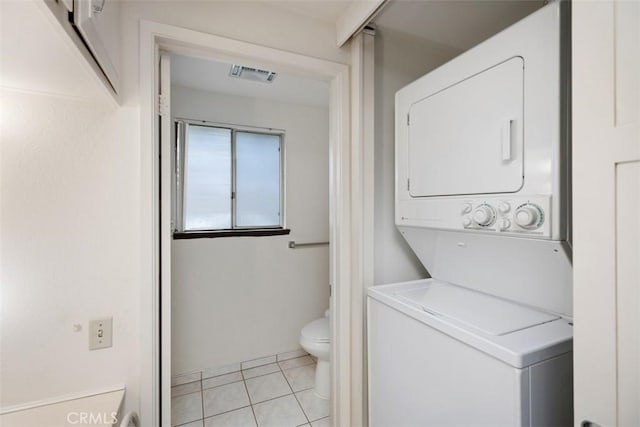 laundry area with stacked washer / dryer and light tile patterned flooring