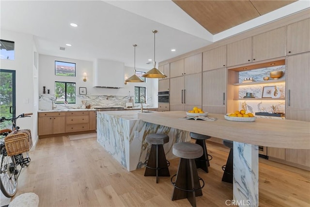 kitchen with light brown cabinetry, decorative light fixtures, lofted ceiling, decorative backsplash, and light wood-type flooring