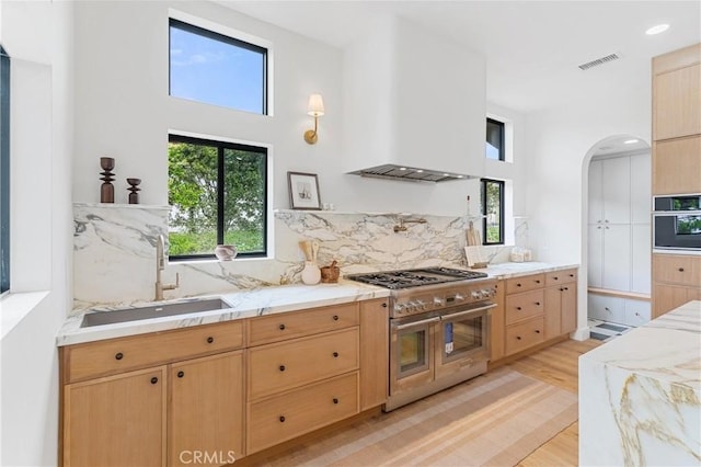 kitchen with sink, range hood, tasteful backsplash, light hardwood / wood-style floors, and range with two ovens