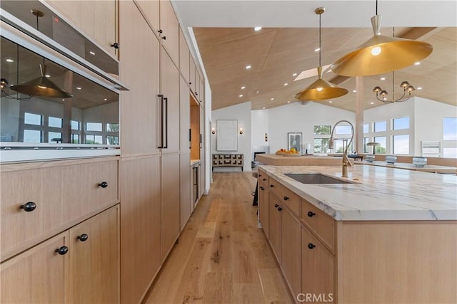 kitchen featuring light brown cabinetry, vaulted ceiling, light wood-type flooring, a large island with sink, and light stone countertops