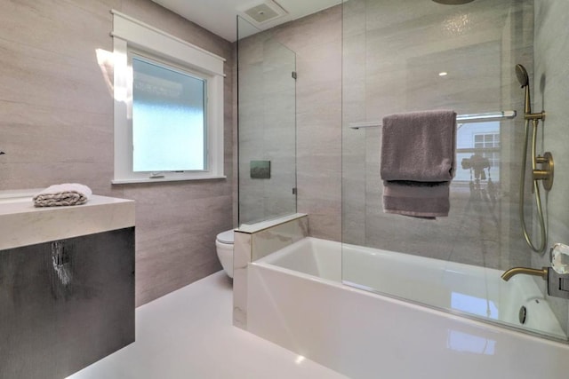 bathroom featuring toilet, combined bath / shower with glass door, and tile walls