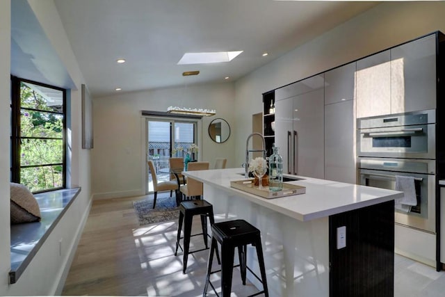 kitchen featuring a kitchen bar, lofted ceiling with skylight, an island with sink, and light wood-type flooring