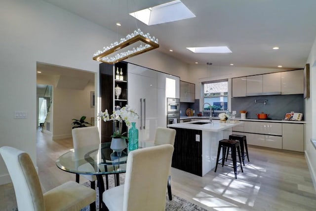 kitchen with lofted ceiling with skylight, sink, a kitchen breakfast bar, a center island with sink, and light wood-type flooring