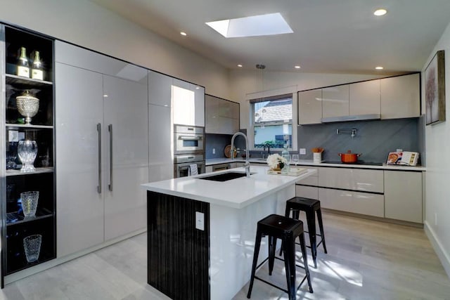 kitchen featuring lofted ceiling with skylight, double oven, sink, a breakfast bar area, and a center island with sink