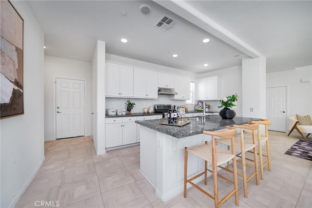 kitchen featuring stainless steel electric range oven, backsplash, white cabinets, a kitchen breakfast bar, and dark stone counters