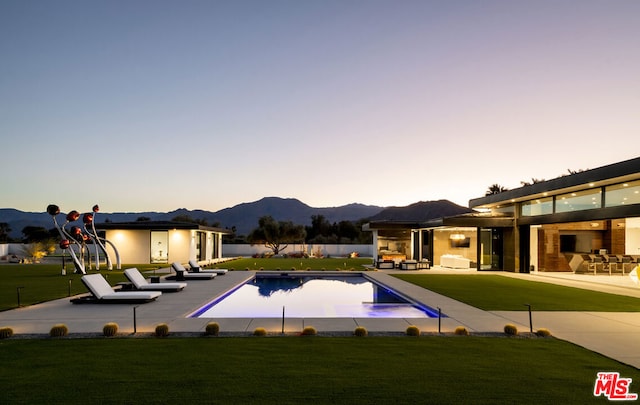 pool at dusk featuring a mountain view, a lawn, and a patio