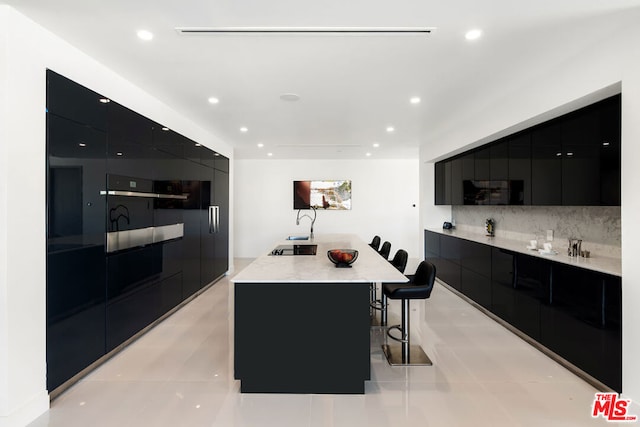 kitchen featuring tasteful backsplash, a breakfast bar, light tile patterned floors, and a large island with sink