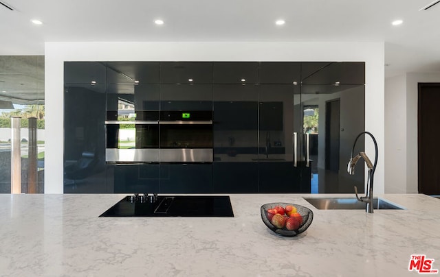 kitchen with stainless steel oven, black electric stovetop, light stone countertops, and sink