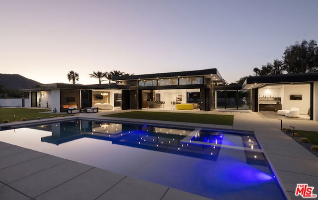 pool at dusk with an outdoor living space, an outdoor kitchen, and a patio area