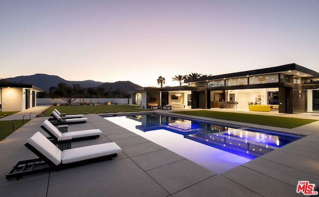 pool at dusk featuring a mountain view, an outdoor hangout area, a lawn, and a patio area