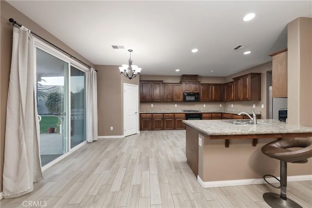 kitchen with sink, a kitchen breakfast bar, hanging light fixtures, kitchen peninsula, and light wood-type flooring