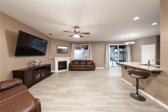 living room with sink, ceiling fan with notable chandelier, and light hardwood / wood-style flooring